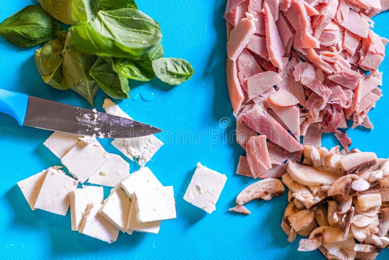 De couper ingr?dients tels que le jambon, le champignon, le fromage et le basilic sur un hachoir de plastique bleu avec un coutea photographie stock De couper ingr?dients tels que le jambon, le champignon, le fromage et le basilic sur un hachoir de plastique bleu avec un coutea photographie stock