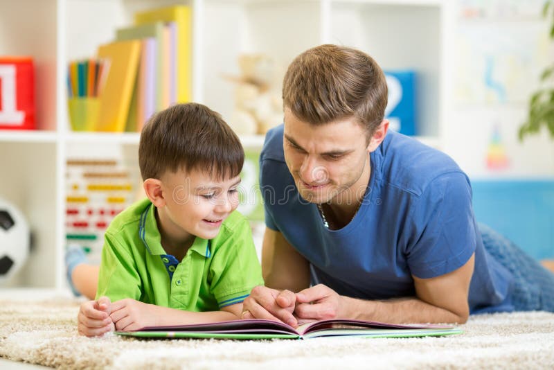 De de kindjongen en papa lezen een boek thuis op vloer stock fotografie De de kindjongen en papa lezen een boek thuis op vloer stock fotografie