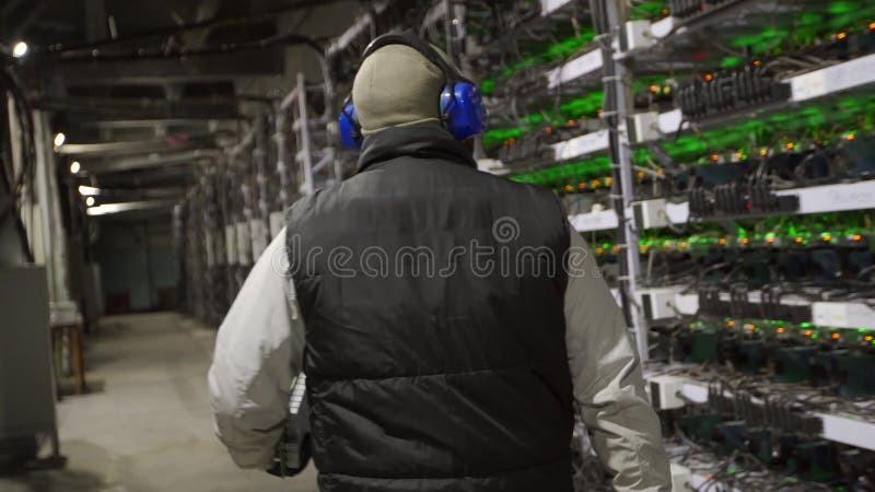 De diagnosetechnicus van het gegevenscentrum loopt langs de mijnbouwmateriaalrekken in serverruimte. de controles van de netwerkbe