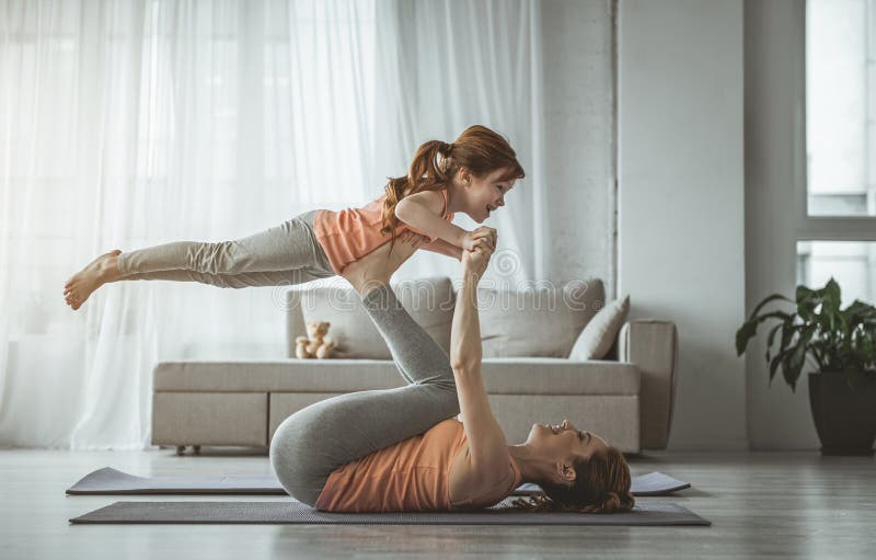 Little bird. Mother is lying on her back and holding her daughter on her feet during fitness at home. Girl looking happy while women is laughing. Little bird. Mother is lying on her back and holding her daughter on her feet during fitness at home. Girl looking happy while women is laughing