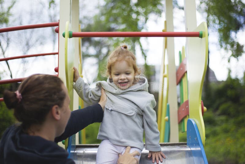 De dochter van moedervangsten van een kinderendia, stelde tevreden dochter op een kinderenspeelplaats tevreden stock foto De dochter van moedervangsten van een kinderendia, stelde tevreden dochter op een kinderenspeelplaats tevreden stock foto