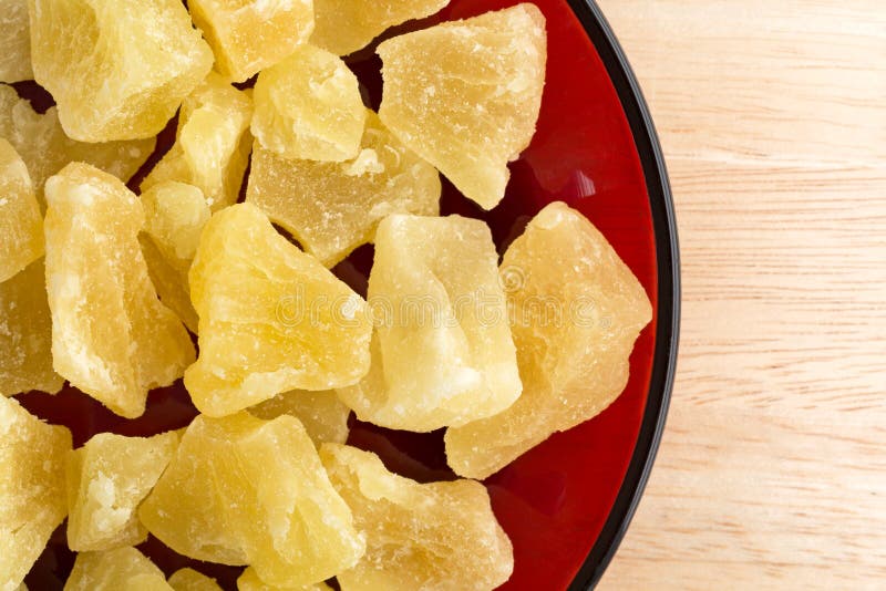 Top close view of a serving of dried sugared pineapple chunks on a red dish atop a wood table top. Top close view of a serving of dried sugared pineapple chunks on a red dish atop a wood table top.