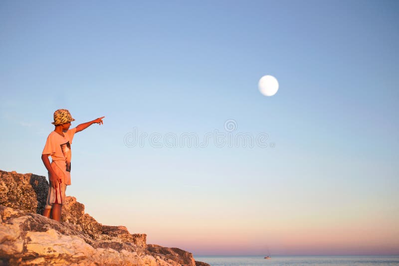 De dromerige jongen richt zijn vinger met de maan in de hemel