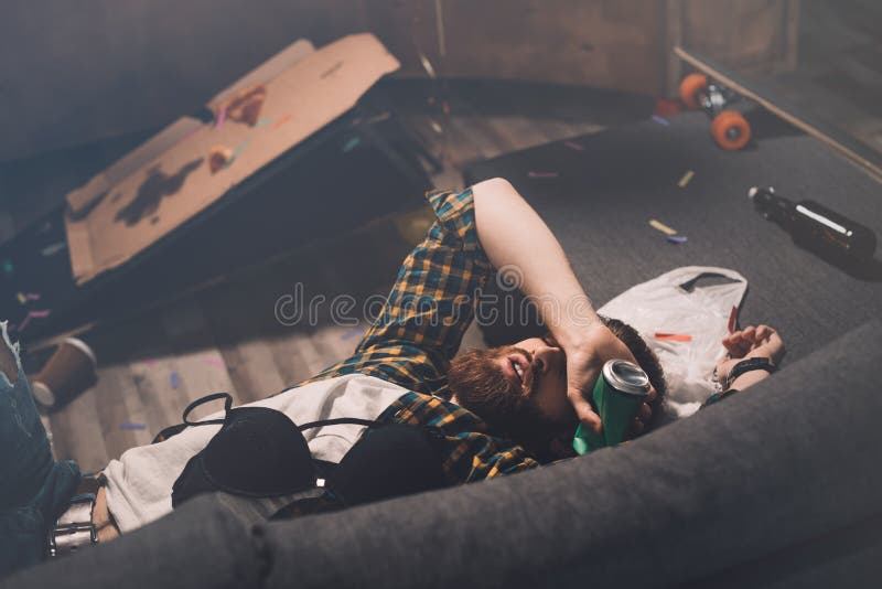 De dronken gebaarde jonge mensenslaap op laag met bustehouder en bier kan stock afbeelding De dronken gebaarde jonge mensenslaap op laag met bustehouder en bier kan stock afbeelding