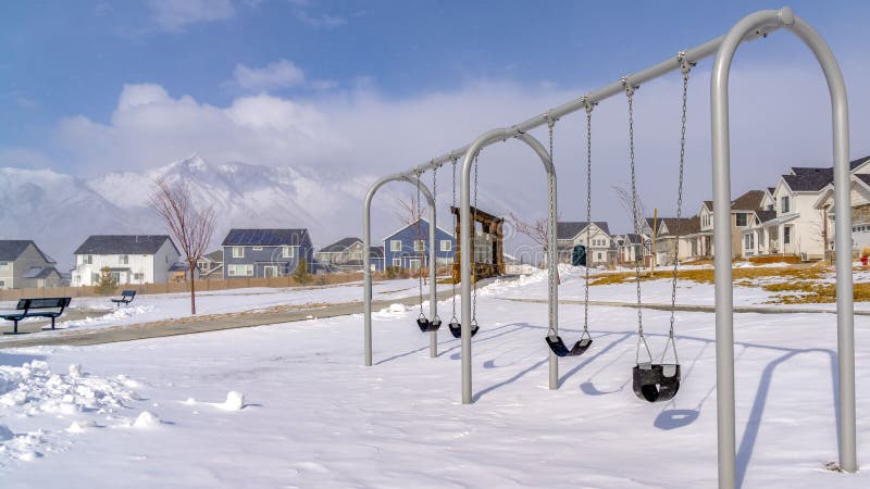 De duidelijke die schommeling van de Panoramababy bij een speelplaats met schone sneeuw op een zonnige de winterdag wordt bedekt stock afbeelding De duidelijke die schommeling van de Panoramababy bij een speelplaats met schone sneeuw op een zonnige de winterdag wordt bedekt stock afbeelding