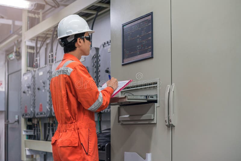 De elektro en Instrumententechnicus die elektrocontrolesystemen van olie en gas controleert verwerkt in de elektroruimte van het stock afbeeldingen De elektro en Instrumententechnicus die elektrocontrolesystemen van olie en gas controleert verwerkt in de elektroruimte van het stock afbeeldingen