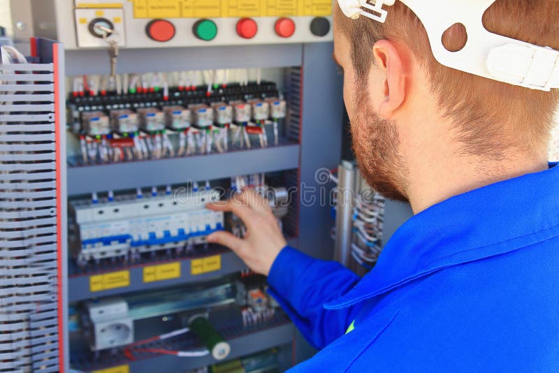 De elektroingenieur voert omschakeling van industrieel materiaal op een vage achtergrond van het controlekabinet uit royalty-vrije stock fotografie De elektroingenieur voert omschakeling van industrieel materiaal op een vage achtergrond van het controlekabinet uit royalty-vrije stock fotografie
