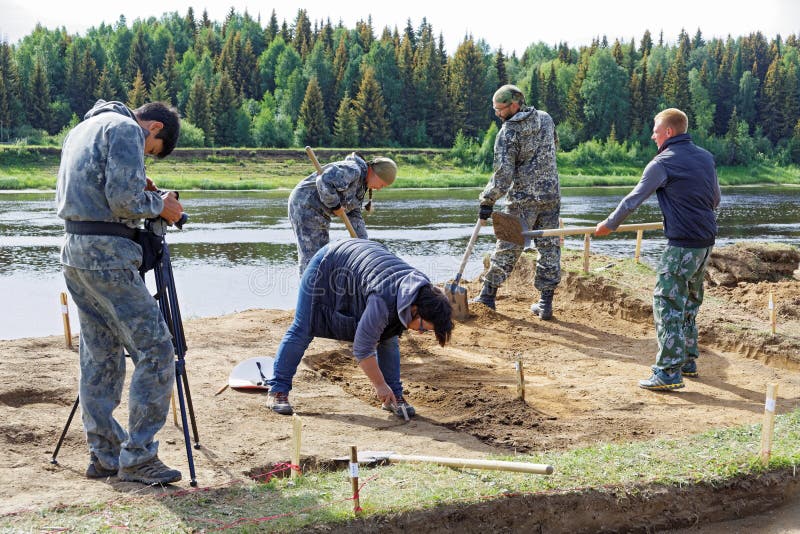 De exploitant neemt een video van een groep mensen die bij de archeologische uitgravingen aan de rivierbank werken stock fotografie De exploitant neemt een video van een groep mensen die bij de archeologische uitgravingen aan de rivierbank werken stock fotografie