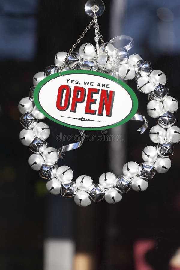 De feestelijke Kerstmisdecoratie en het open teken met de kroon van de kenwijsjeklok het hangen in winkel slaan vensterdeur op Va stock foto's De feestelijke Kerstmisdecoratie en het open teken met de kroon van de kenwijsjeklok het hangen in winkel slaan vensterdeur op Va stock foto's