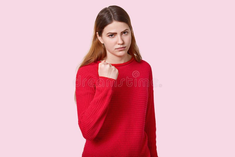 De foto van droevige boze jonge Europese vrouw met recht donker haar, toont vuist bij camera, gekleed in rood verbindingsdraad, s royalty-vrije stock fotografie De foto van droevige boze jonge Europese vrouw met recht donker haar, toont vuist bij camera, gekleed in rood verbindingsdraad, s royalty-vrije stock fotografie