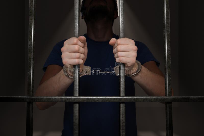 Arrested prisoner is holding bars in prison cell. Arrested prisoner is holding bars in prison cell.
