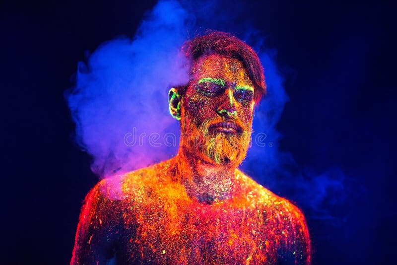 De gebaarde mens schilderde in fluorescent poeder op een achtergrond van rook royalty-vrije stock foto De gebaarde mens schilderde in fluorescent poeder op een achtergrond van rook royalty-vrije stock foto