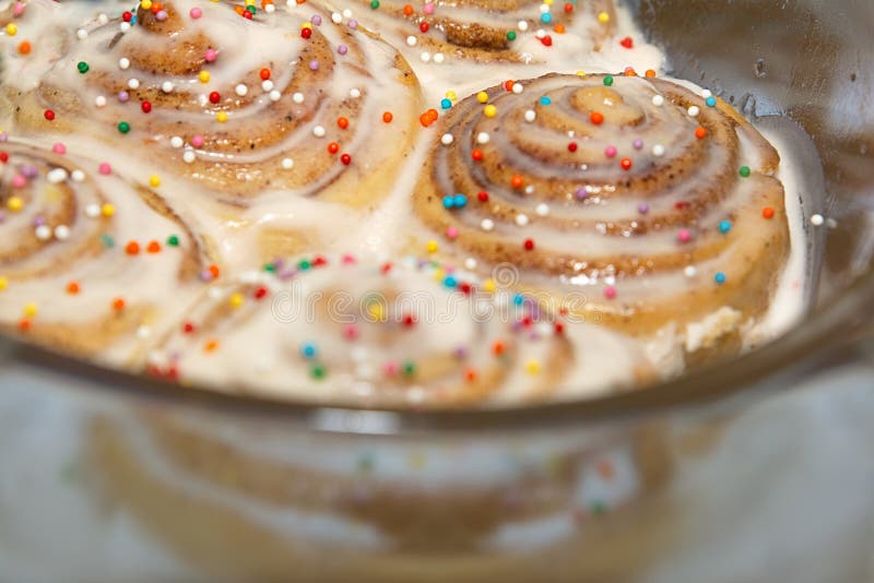 De gebakken kaneelbroodjes zijn doorweekt in suikerglazuur en bestrooid met decoratie zijn in een transparante vorm stock afbeeldingen De gebakken kaneelbroodjes zijn doorweekt in suikerglazuur en bestrooid met decoratie zijn in een transparante vorm stock afbeeldingen