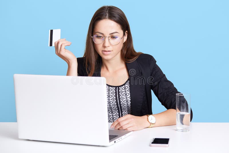 De geconcentreerde bezige zekere vrouw zit in bureau, die met haar laptop werken, opheffend creditcard, bekijkend monitor, die gl royalty-vrije stock foto De geconcentreerde bezige zekere vrouw zit in bureau, die met haar laptop werken, opheffend creditcard, bekijkend monitor, die gl royalty-vrije stock foto