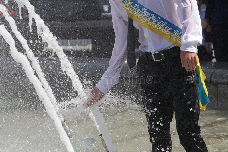 Graduate bathes in a fountain after finishing school. Inscription on the tape `Graduate` in Ukrainian. Graduate bathes in a fountain after finishing school. Inscription on the tape `Graduate` in Ukrainian