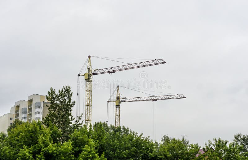 De gele kraan is de bouw, behing de bomen, dichtbijgelegen huizen, sterft de aard stock afbeelding De gele kraan is de bouw, behing de bomen, dichtbijgelegen huizen, sterft de aard stock afbeelding