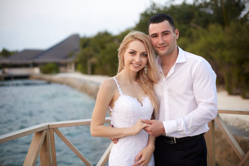 De gelukkige bruid en bruidegom die en handen op een tropisch strand van luxury spa glimlachen de houden nemen op de Maldiven zij stock fotografie De gelukkige bruid en bruidegom die en handen op een tropisch strand van luxury spa glimlachen de houden nemen op de Maldiven zij stock fotografie