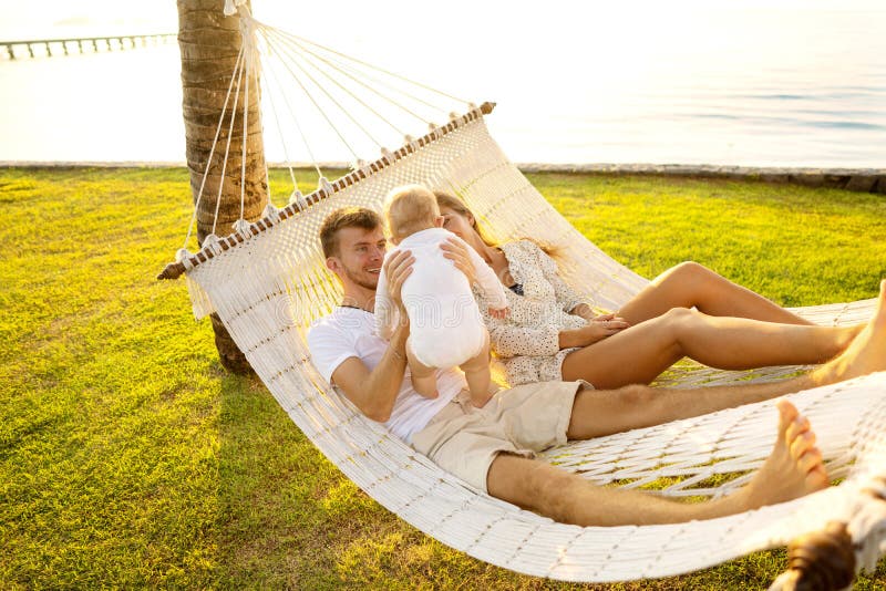 De gelukkige familie op een tropisch eiland bij zonsondergang ligt in een hangmat en speelt met hun zoon stock afbeeldingen De gelukkige familie op een tropisch eiland bij zonsondergang ligt in een hangmat en speelt met hun zoon stock afbeeldingen