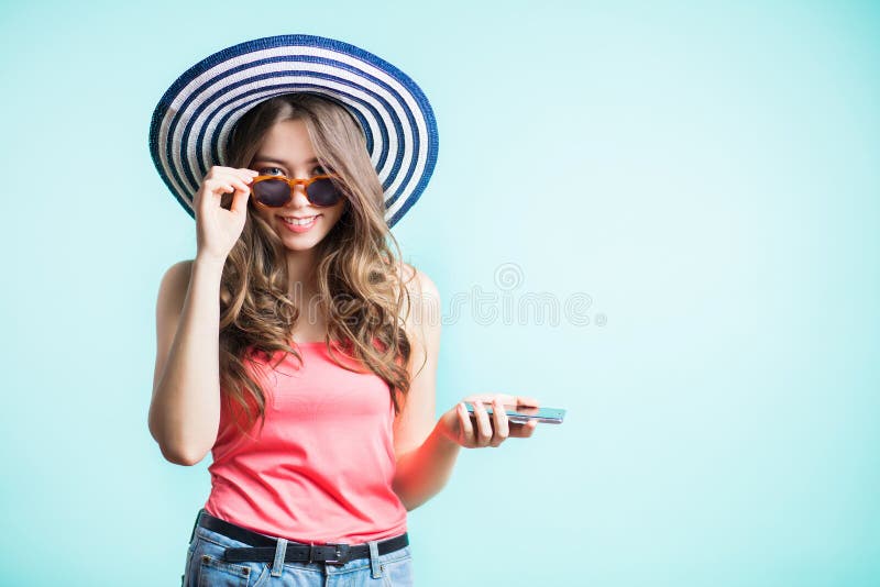 De gelukkige glimlachende vrouw in zonnebril en een hoed die de camera onderzoeken, houden haar hand op smartphone royalty-vrije stock fotografie De gelukkige glimlachende vrouw in zonnebril en een hoed die de camera onderzoeken, houden haar hand op smartphone royalty-vrije stock fotografie