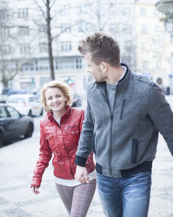 De gelukkige jonge handen van de paarholding terwijl het lopen op stadsstraat royalty-vrije stock afbeelding De gelukkige jonge handen van de paarholding terwijl het lopen op stadsstraat royalty-vrije stock afbeelding