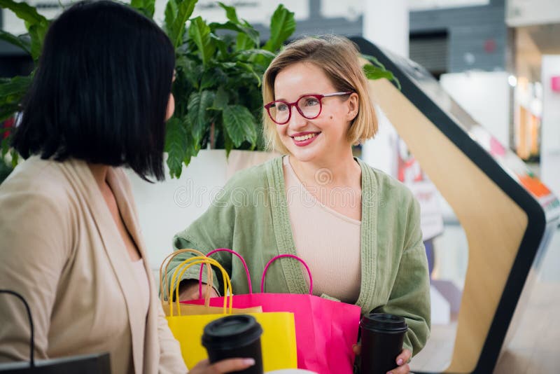 De gelukkige jonge vrouwen met het winkelen zakken en koffiedocument vormt het zitten tot een kom, het rusten en het spreken na h royalty-vrije stock foto's De gelukkige jonge vrouwen met het winkelen zakken en koffiedocument vormt het zitten tot een kom, het rusten en het spreken na h royalty-vrije stock foto's