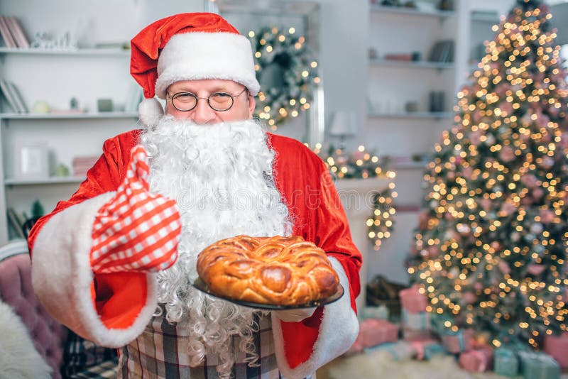 De gelukkige mens in Santa Claus-kleren houdt pastei en toont grote duim De kerel kijkt op camera Hij is in feestelijke alleen ru royalty-vrije stock afbeeldingen De gelukkige mens in Santa Claus-kleren houdt pastei en toont grote duim De kerel kijkt op camera Hij is in feestelijke alleen ru royalty-vrije stock afbeeldingen
