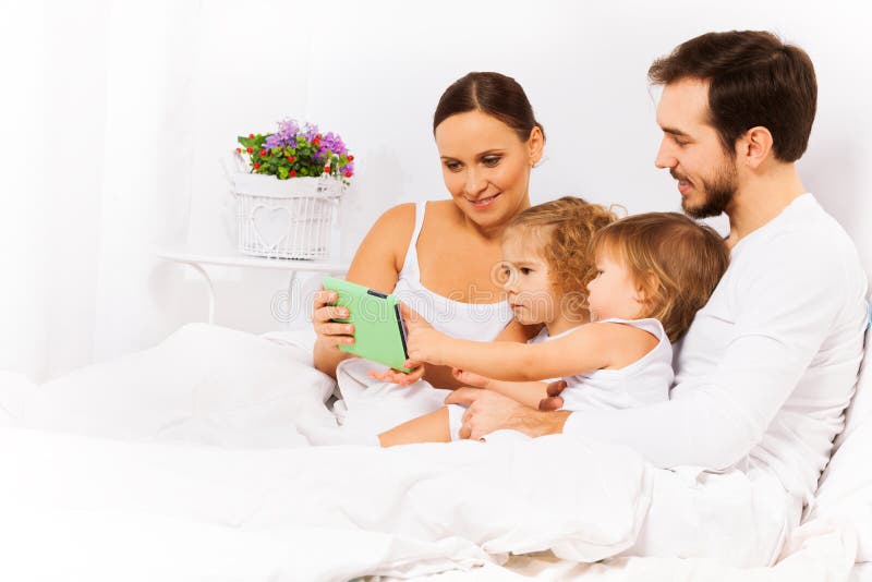 De gelukkige ouders met twee jonge geitjes bekijken tablet stock foto's De gelukkige ouders met twee jonge geitjes bekijken tablet stock foto's