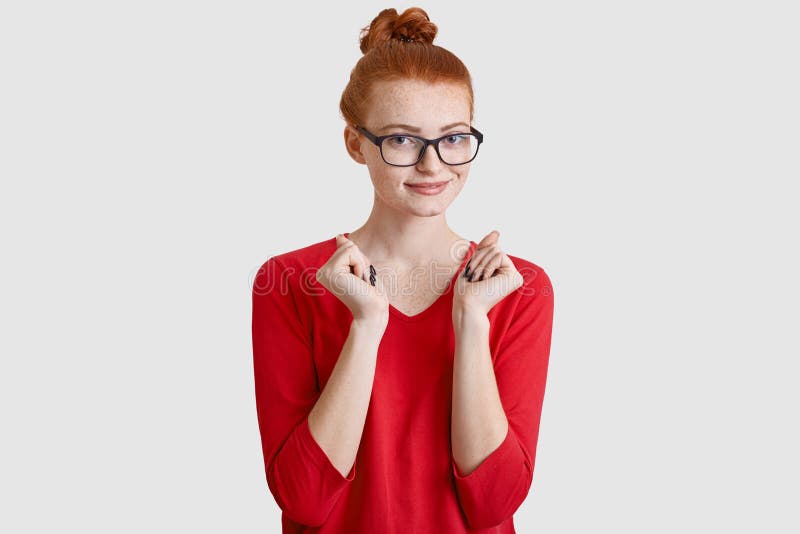 De gelukkige rode haired freckled jonge vrouw met knoop houdt handen gedrukt, wacht op iets met intrige, kijkt door transparant royalty-vrije stock fotografie De gelukkige rode haired freckled jonge vrouw met knoop houdt handen gedrukt, wacht op iets met intrige, kijkt door transparant royalty-vrije stock fotografie