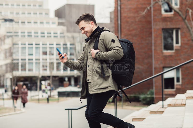 De gelukkige tekst van de studentenmens op celtelefoon die in de campus van de stadsuniversiteit met rugzak lopen stock foto's De gelukkige tekst van de studentenmens op celtelefoon die in de campus van de stadsuniversiteit met rugzak lopen stock foto's