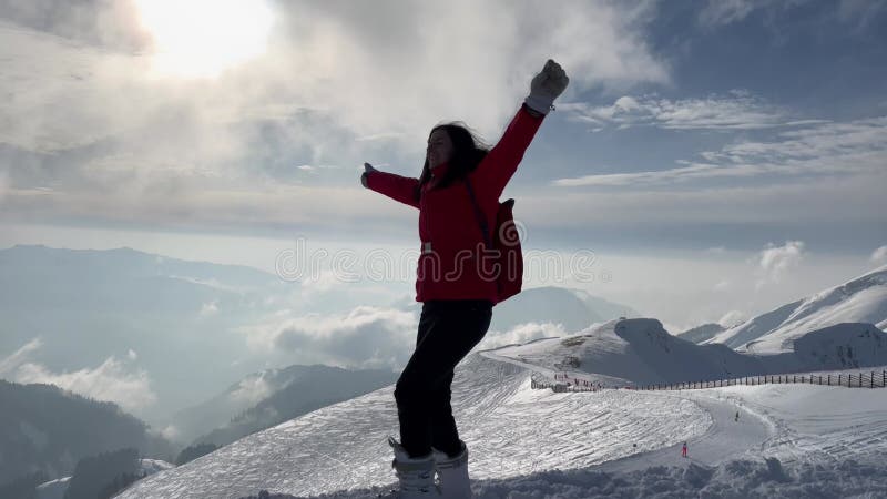 De gelukkige vrouw bovenop de sneeuwberg in de winter trekt haar handen op uit het succes