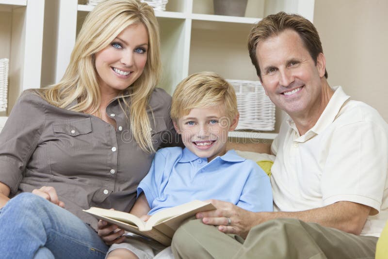 De gelukkige Zitting van de Familie op Bank die een Boek leest stock fotografie De gelukkige Zitting van de Familie op Bank die een Boek leest stock fotografie