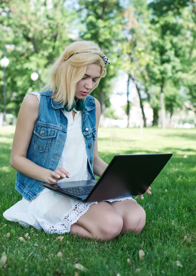 De gemengde zitting van de rasstudent op het gras die aan laptop werken stock foto De gemengde zitting van de rasstudent op het gras die aan laptop werken stock foto