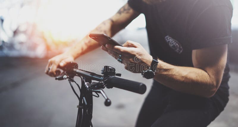 De getatoeeerde hipster mens in holdingssmartphone handen en het gebruiken brengt app in kaart alvorens door elektrische autoped stock afbeelding De getatoeeerde hipster mens in holdingssmartphone handen en het gebruiken brengt app in kaart alvorens door elektrische autoped stock afbeelding