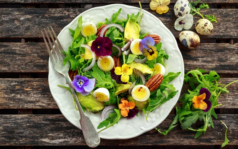 De gezonde de zomersalade met kwartelseieren, avocado, pecannoten, wilde raket, rode ui en eetbare altviool bloeit stock afbeelding De gezonde de zomersalade met kwartelseieren, avocado, pecannoten, wilde raket, rode ui en eetbare altviool bloeit stock afbeelding