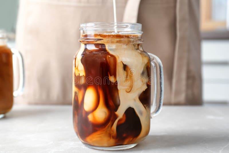 De gietende melk in metselaarkruik met koude brouwt koffie royalty-vrije stock afbeeldingen De gietende melk in metselaarkruik met koude brouwt koffie royalty-vrije stock afbeeldingen