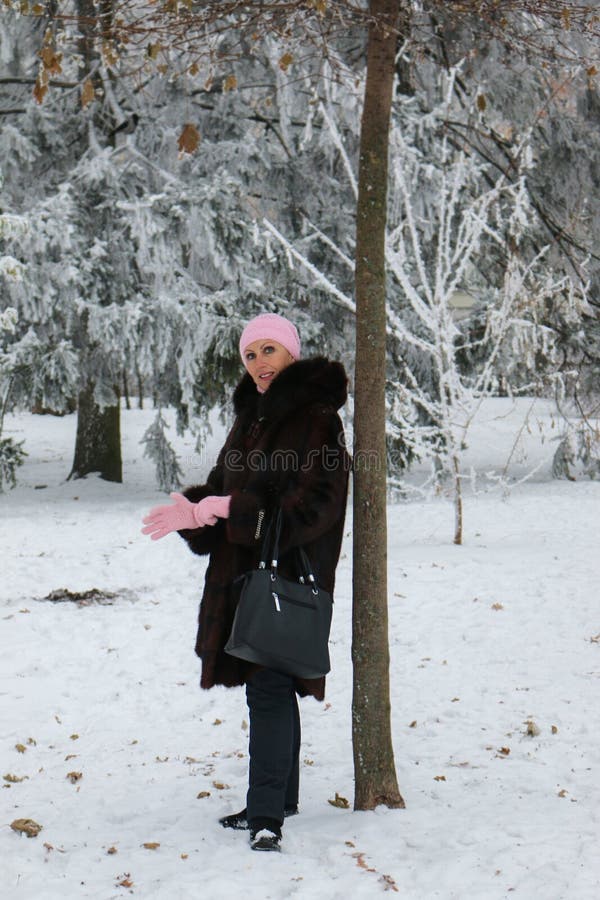 De glimlachende vrouw in bontjas blijft dichtbij de boom in park stock fotografie De glimlachende vrouw in bontjas blijft dichtbij de boom in park stock fotografie