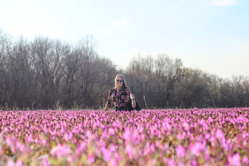 De glimlachende vrouw met glazen zit op een gebied van vroege de lente wildflowerswith naakte bomen achter haar - selectieve nadr royalty-vrije stock fotografie De glimlachende vrouw met glazen zit op een gebied van vroege de lente wildflowerswith naakte bomen achter haar - selectieve nadr royalty-vrije stock fotografie