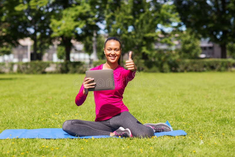 Fitness, park, technology, gesture and people concept - smiling african american woman with tablet pc showing thumbs up outdoors. Fitness, park, technology, gesture and people concept - smiling african american woman with tablet pc showing thumbs up outdoors.