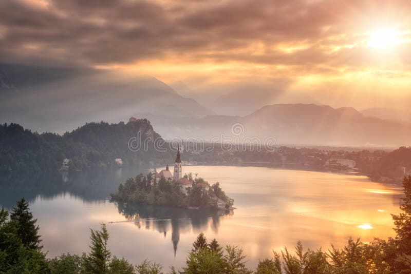 De gouden zonsopgang over beroemd alpien meer tapte met Veronderstelling van de bedevaartkerk van Mary af op het eiland, Slovenië stock afbeelding De gouden zonsopgang over beroemd alpien meer tapte met Veronderstelling van de bedevaartkerk van Mary af op het eiland, Slovenië stock afbeelding