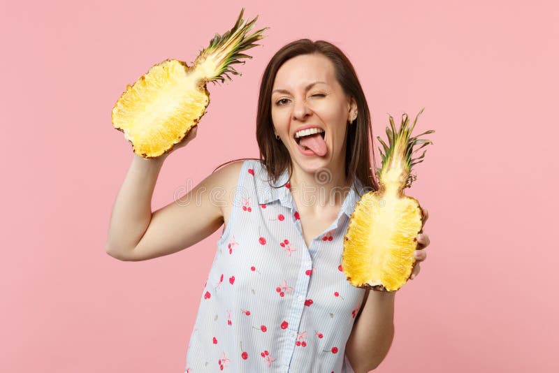 De grappige jonge vrouw in de zomer kleedt het tonen van tongholding halfs van vers rijp die ananasfruit op roze pastelkleur word royalty-vrije stock fotografie De grappige jonge vrouw in de zomer kleedt het tonen van tongholding halfs van vers rijp die ananasfruit op roze pastelkleur word royalty-vrije stock fotografie