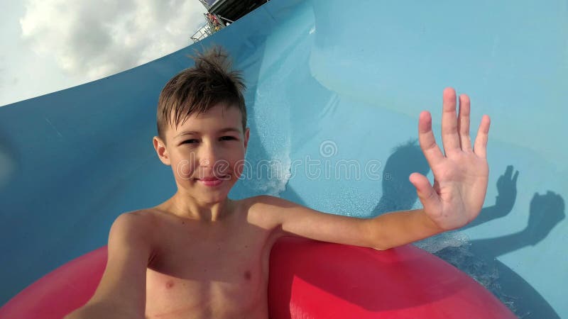 De grappige jongen daalt op de waterdia in het waterpark onderzoekt de camera royalty-vrije stock foto De grappige jongen daalt op de waterdia in het waterpark onderzoekt de camera royalty-vrije stock foto