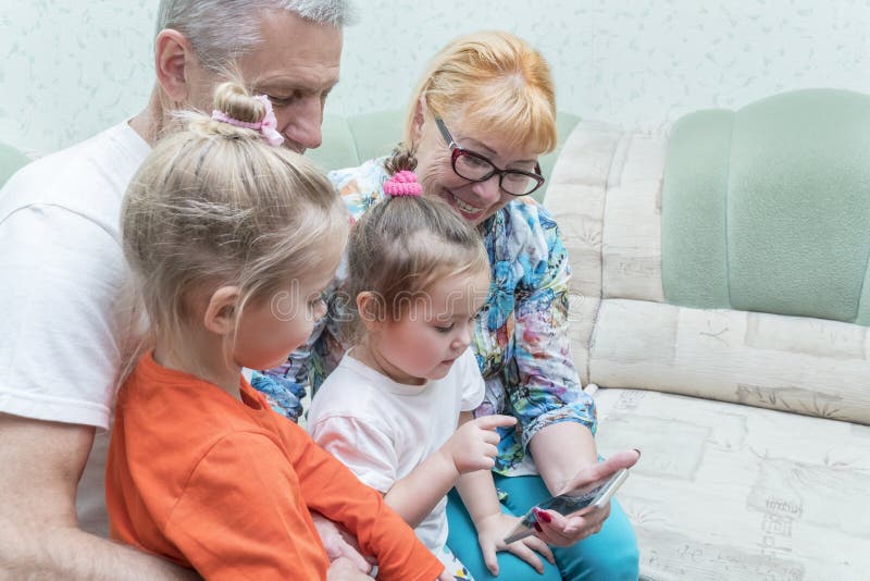 De grootouders en de kleinkinderen bekijken de telefoon stock afbeelding De grootouders en de kleinkinderen bekijken de telefoon stock afbeelding