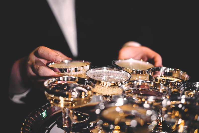 De hand die van het mannetje glanzende gouden glazen champagne in een donkere ruimte houden stock foto De hand die van het mannetje glanzende gouden glazen champagne in een donkere ruimte houden stock foto