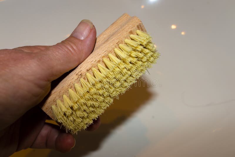De hand houdt een houten borstel met gele borstels voor een lichte achtergrond vast stock afbeelding De hand houdt een houten borstel met gele borstels voor een lichte achtergrond vast stock afbeelding