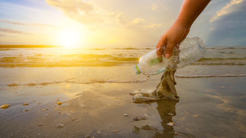 De hand pakt afval op het strand op, het idee van milieubehoud
