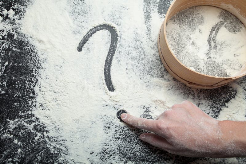 De hand van een vrouw trekt een vraagteken op bloem Zeef voor bloem en het concept eigengemaakte cakes royalty-vrije stock afbeelding De hand van een vrouw trekt een vraagteken op bloem Zeef voor bloem en het concept eigengemaakte cakes royalty-vrije stock afbeelding