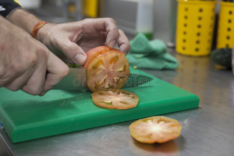 De handen die van Chef roze tomaat in plakken snijden die een scherp mes gebruiken stock foto De handen die van Chef roze tomaat in plakken snijden die een scherp mes gebruiken stock foto