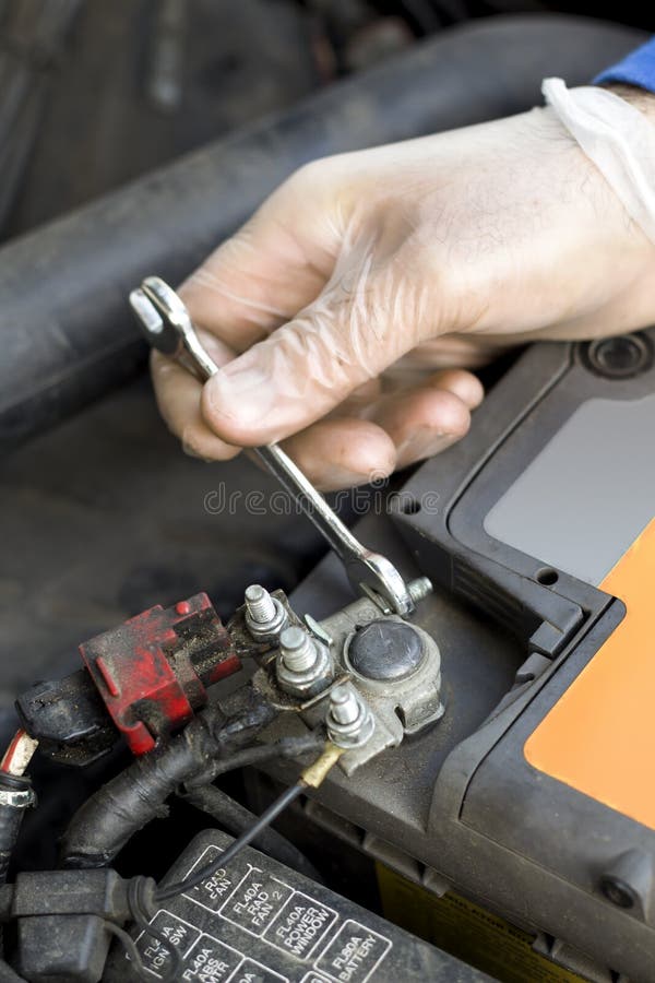 De handen van de autowerktuigkundige in beschikbare handschoenen schroeven de batterijkoppeling los stock fotografie De handen van de autowerktuigkundige in beschikbare handschoenen schroeven de batterijkoppeling los stock fotografie