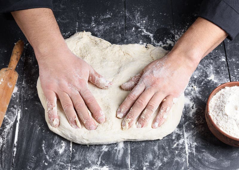 De handen van mensen kneden een rond stuk van deeg voor het maken van pizza stock afbeelding De handen van mensen kneden een rond stuk van deeg voor het maken van pizza stock afbeelding