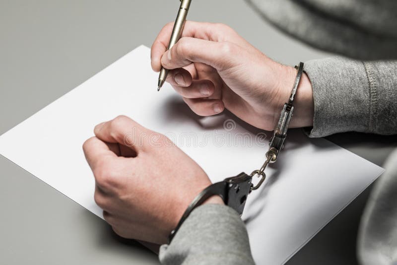 De handen van de misdadiger in handcuffs schrijven een handvat op papier Sinc stock afbeeldingen De handen van de misdadiger in handcuffs schrijven een handvat op papier Sinc stock afbeeldingen